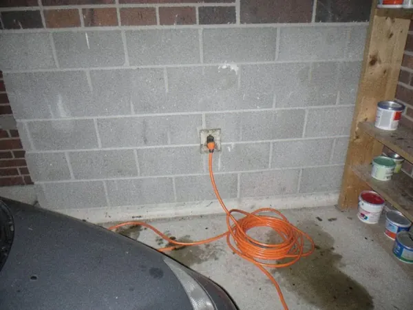 Avant : voiture électrique rechargée sur une rallonge orange branchée à une prise ordinaire du garage.