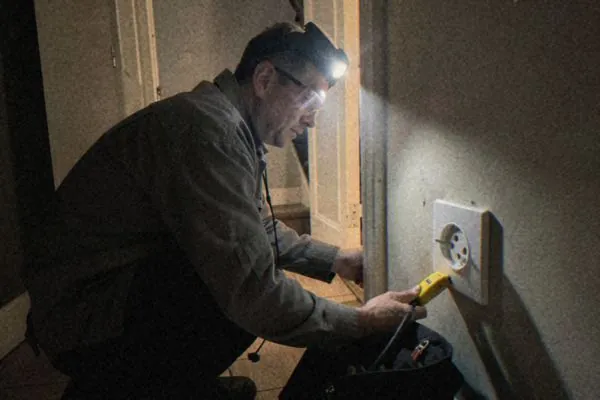 De nuit, à la lampe frontale, un électricien branche un testeur sur une prise pendant une coupure de courant.