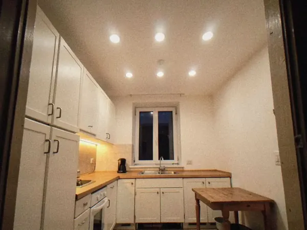 Après : même cuisine avec des spots encastrés au plafond et un ruban LED sous les meubles hauts.
